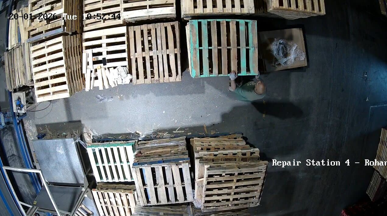 Top-down camera view of a pallet repair station showing the work area, pallets, and employee clearly visible from above